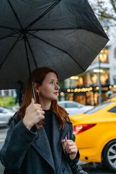 Young woman with red hair holds umbrella in rainy Ankara street, showcasing urban fashion.