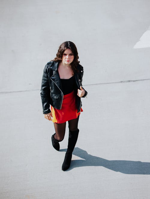 Young girl wearing a black leather jacket and red skirt walking 