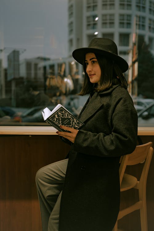 Woman in Black Sitting on High Chair with Open Book in Hand