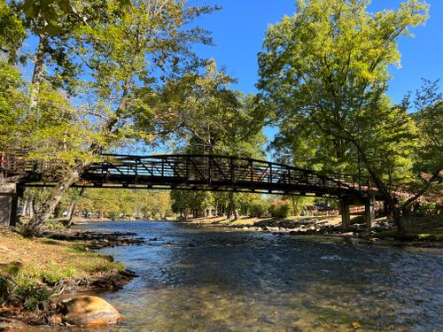 Free Peaceful view of a wooden bridge crossing a river in Oconaluftee Island Park, surrounded by lush trees. Stock Photo