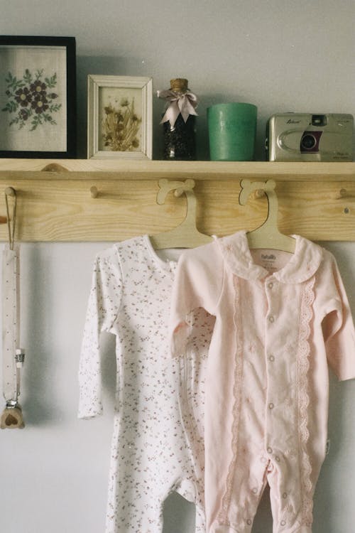 Baby Rompers on Hangers Under a Shelf with Framed Pictures and an Old Camera