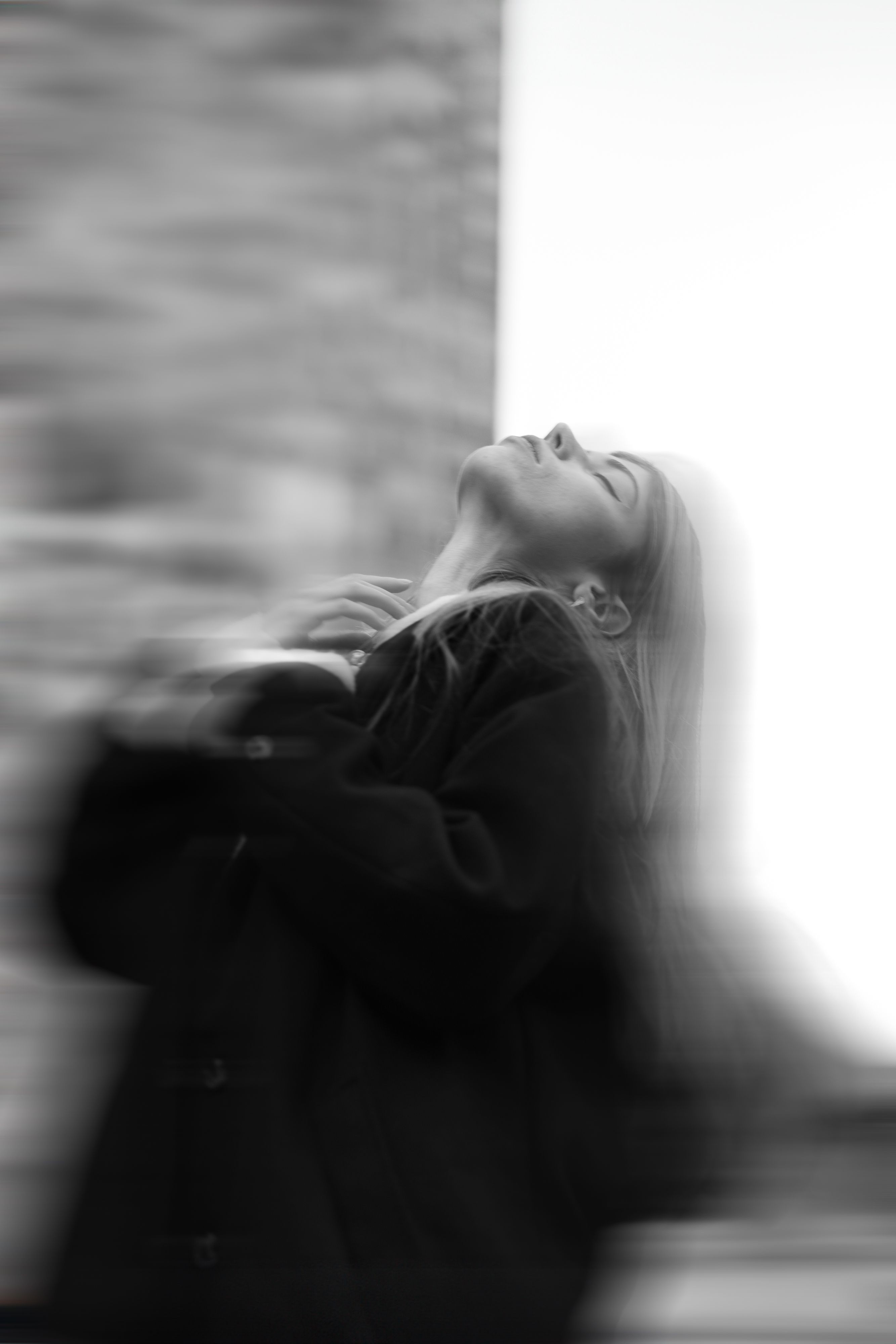A blurred black and white portrait of a woman in a contemplative pose with eyes closed.