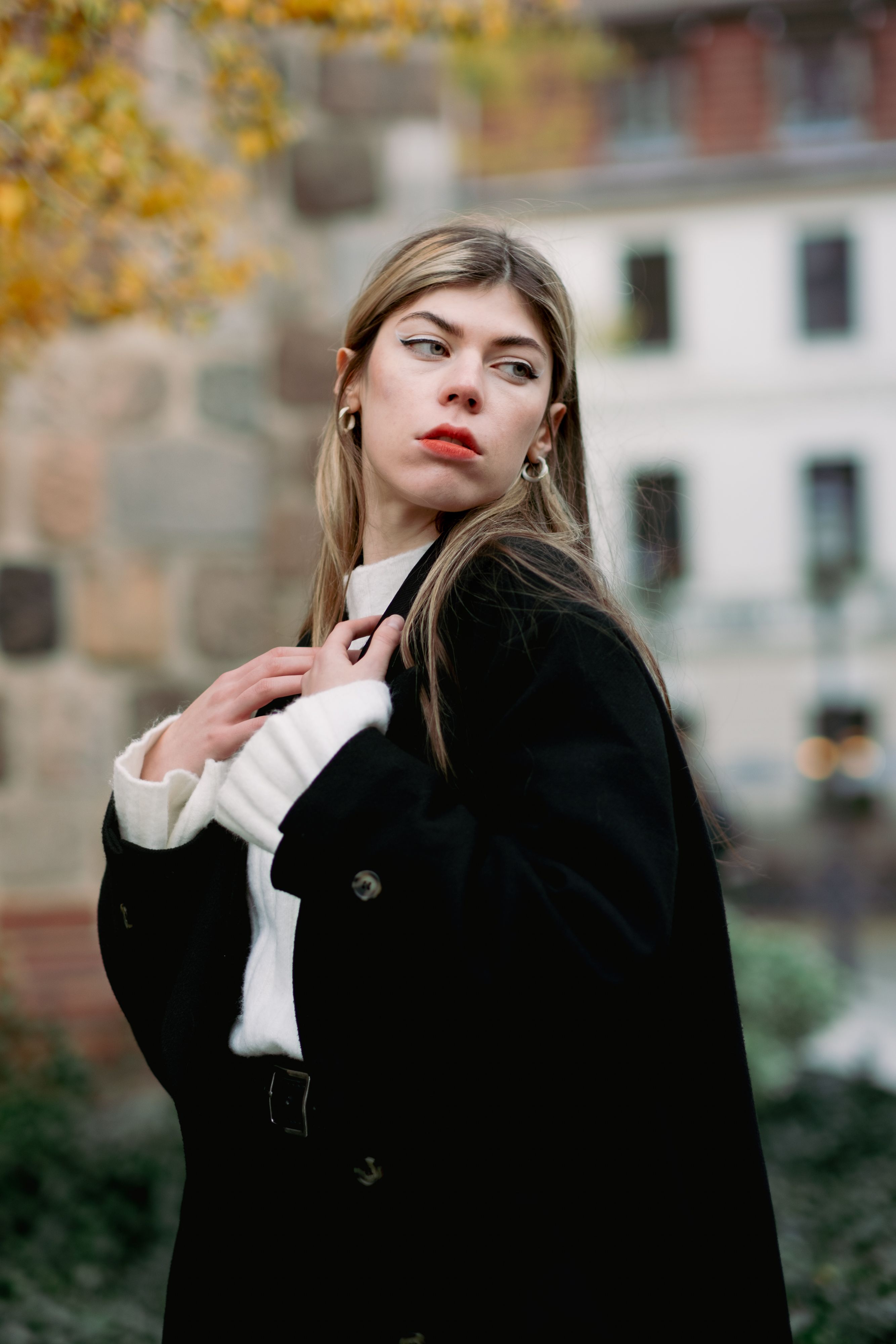 A fashionable woman in a black coat posing thoughtfully in an urban autumn environment.