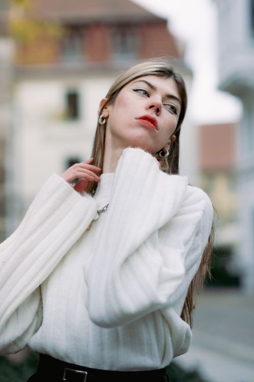 Free Portrait of a fashionable woman in a white sweater posing outdoors with a blurred background. Stock Photo