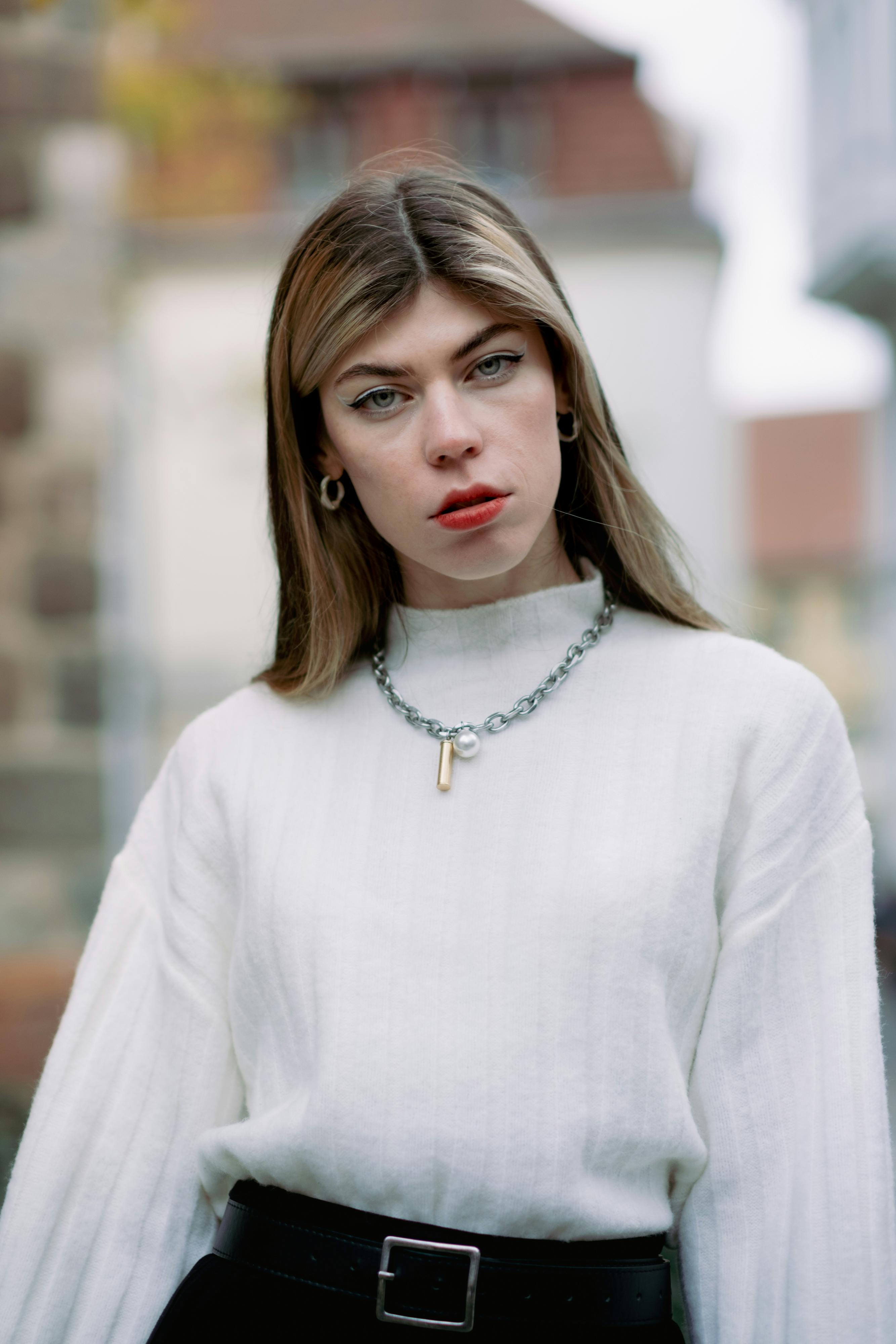 Portrait of a fashionable young woman with red lips in a city backdrop wearing a white sweater.