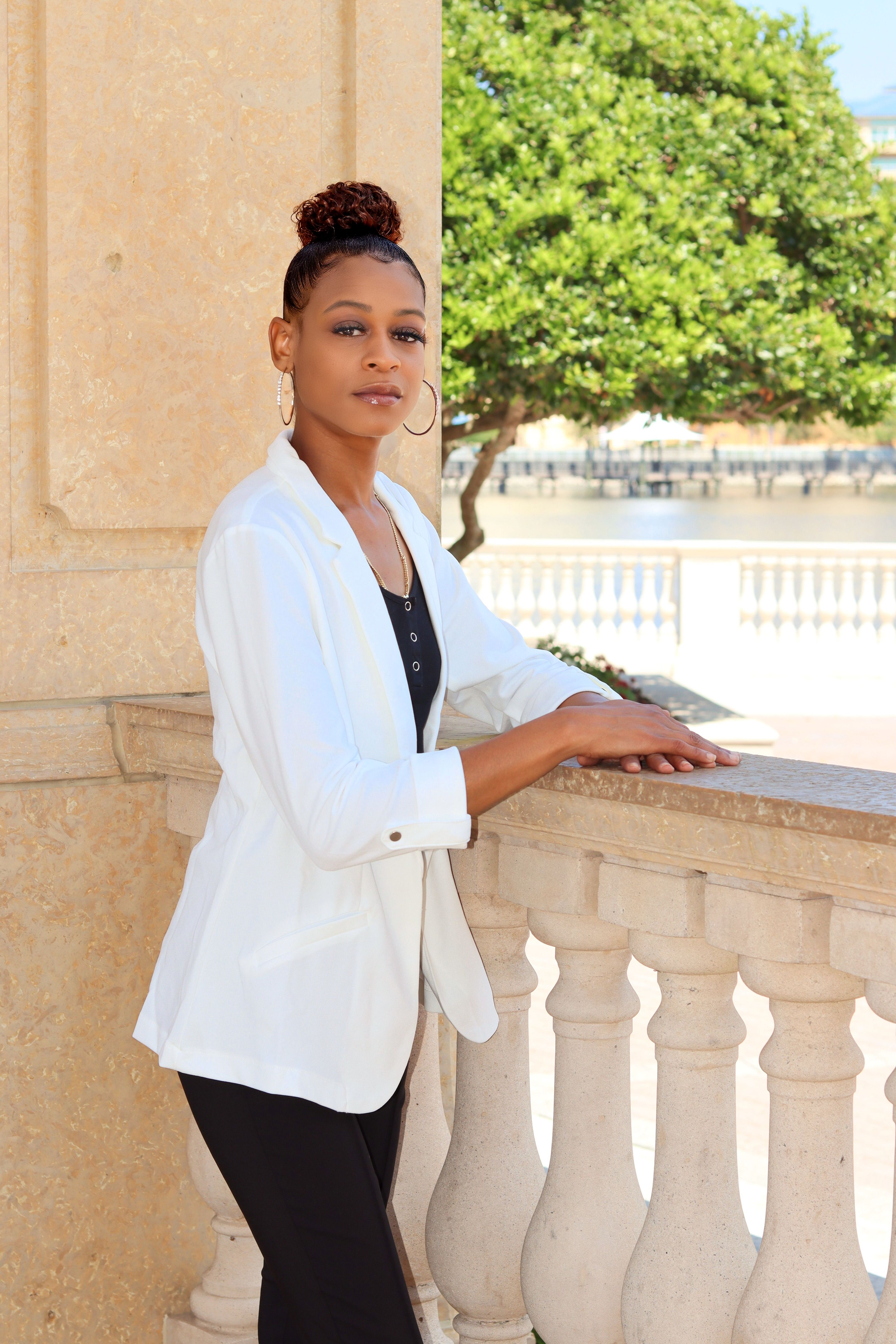 Fashionable businesswoman in white blazer standing on a sunny terrace with elegant surroundings.