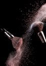 在黑暗背景下，高速捕捉化妆刷分散粉红色粉末的运动
