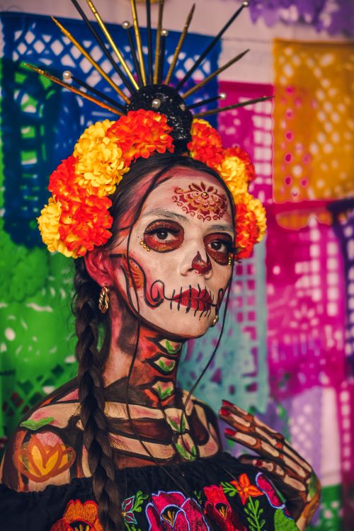 Free Vibrant Day of the Dead Catrina with intricate makeup and floral headpiece against colorful backdrop. Stock Photo