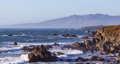 Free Dramatic rocky coastline with waves crashing under clear sky, perfect for nature lovers. Stock Photo