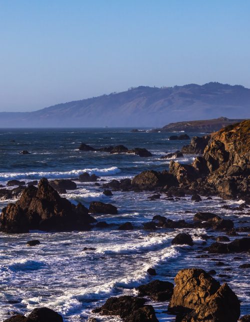 Free Rugged coastal scene with eroded cliffs and crashing waves under a clear sky. Stock Photo