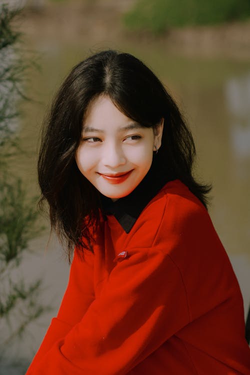 Smiling Model in a Red Sweatshirt over a Black Blouse Sitting by the River