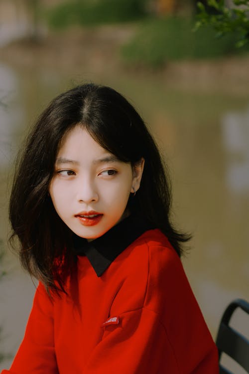 Young Beautiful Woman in a Red Sweatshirt Sitting by the River