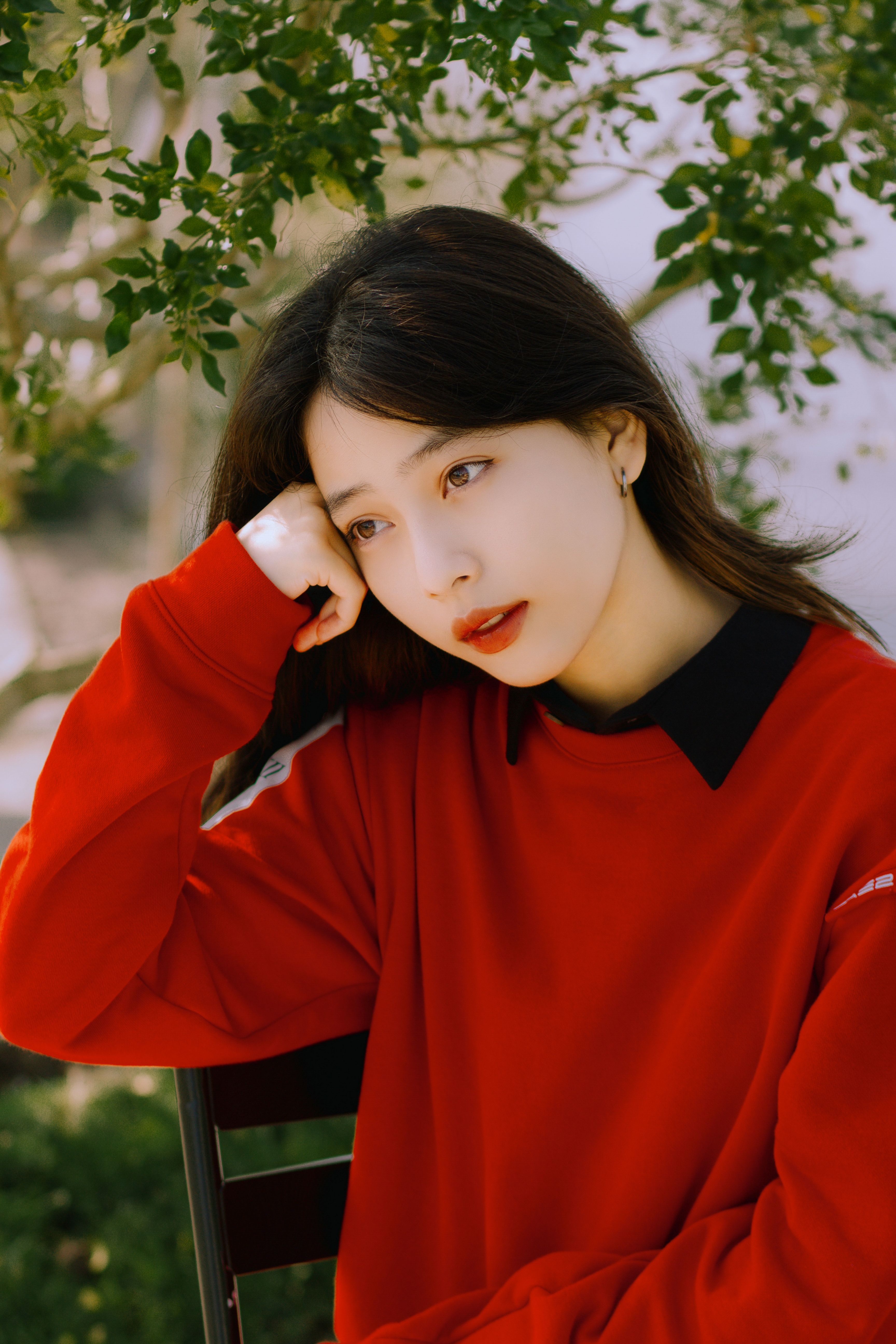 Serene portrait of a woman in a vibrant red blouse sitting outdoors, under natural light.