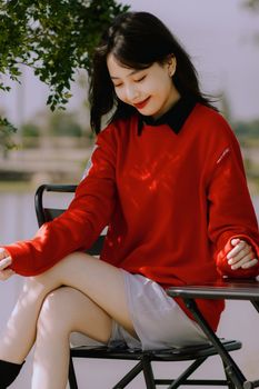 Stylish woman with red lips in a red sweatshirt sitting and smiling by a table outdoors.