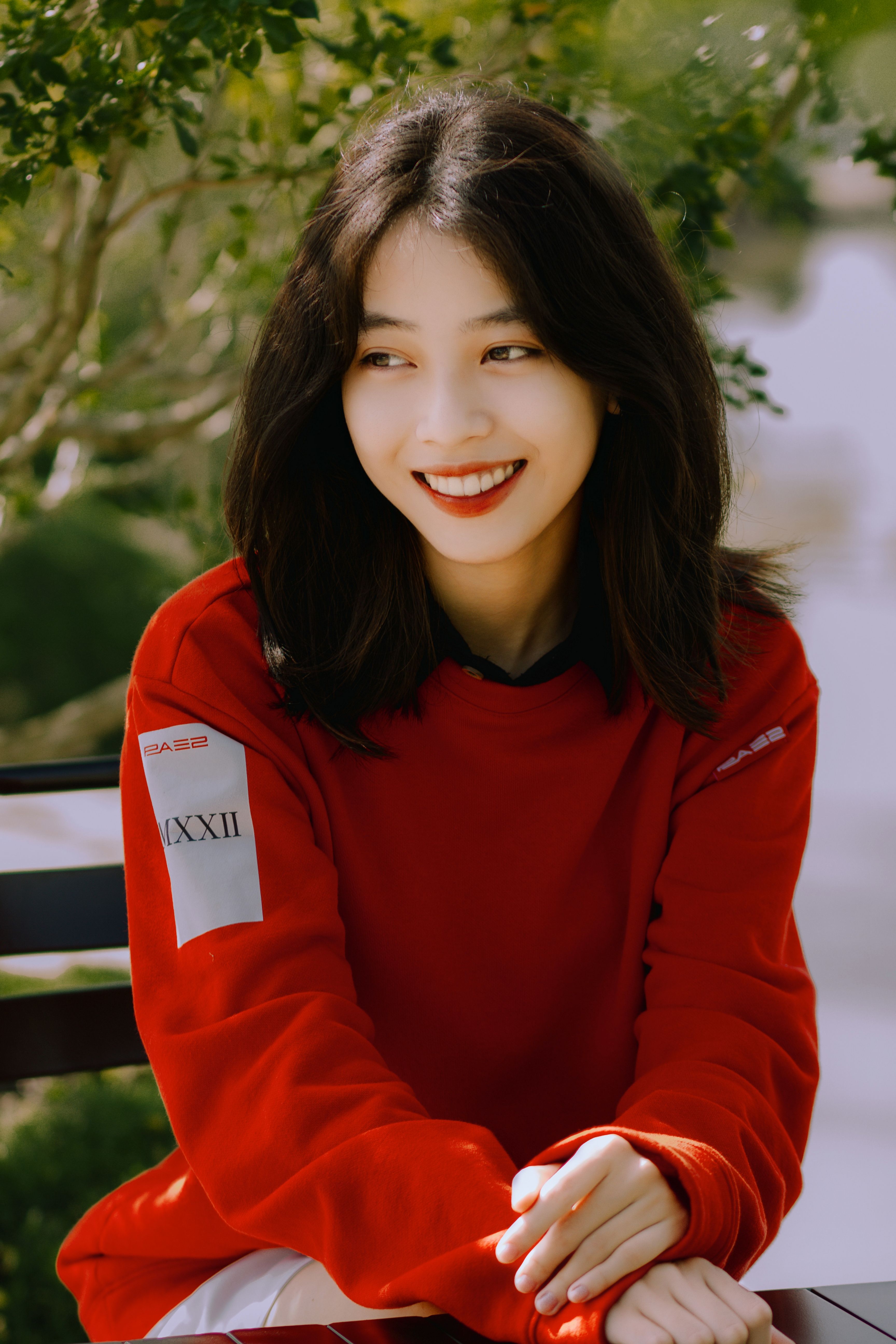 Portrait of a smiling woman in a red sweater enjoying a sunny day outdoors.