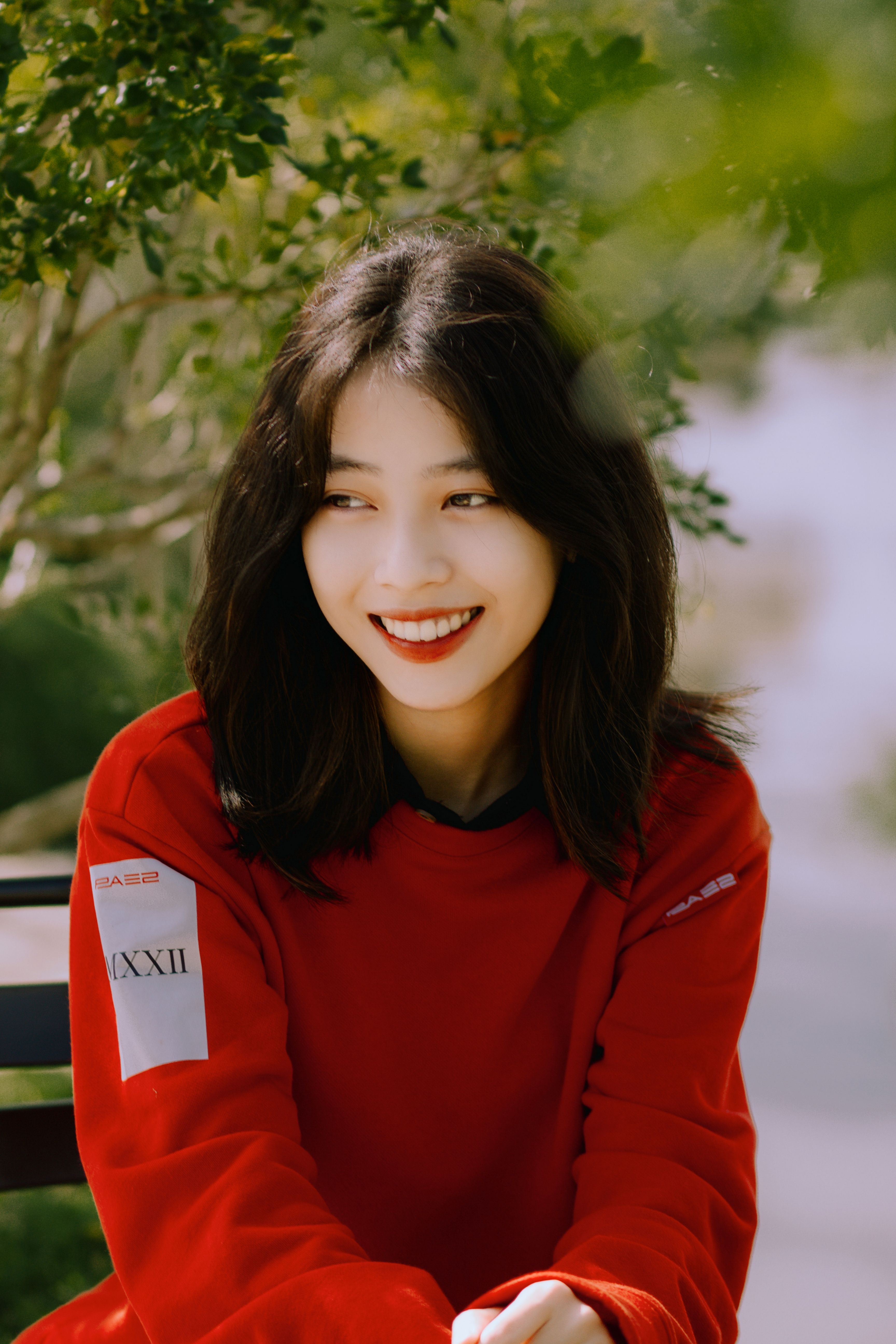 Portrait of a smiling woman in red sweater sitting outdoors on a sunny day.