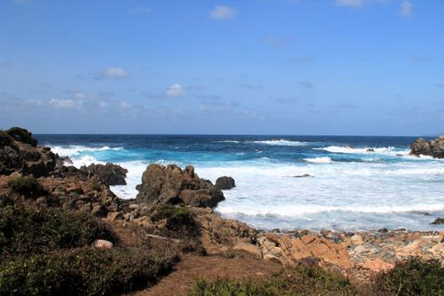 Free A scenic view of a rocky ocean shoreline with waves crashing and a clear blue sky above. Stock Photo