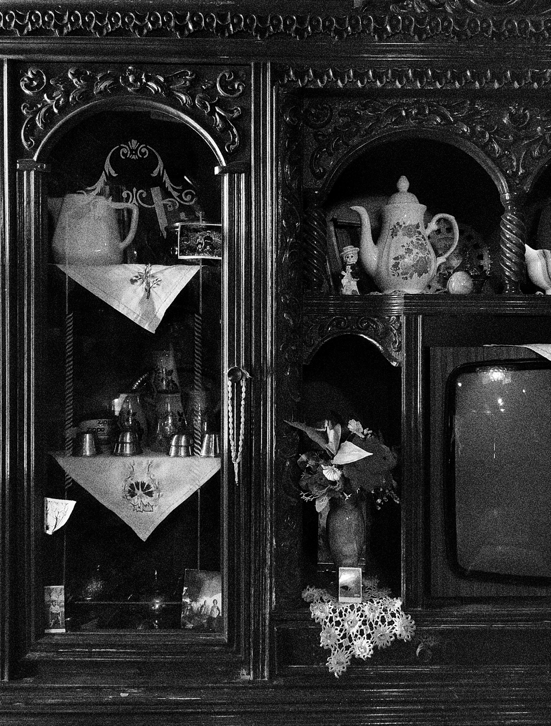 Monochrome photograph of a carved display cabinet with shaped openings, tableware and small ornaments