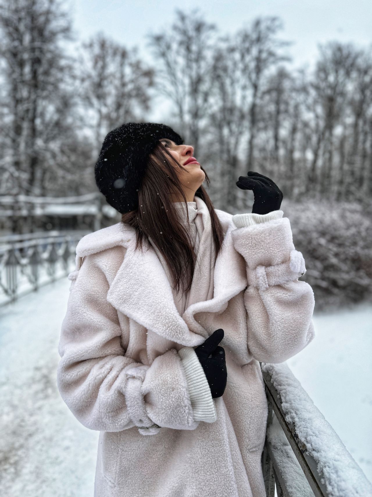 Woman in a plush cream coat enjoying snow in a park