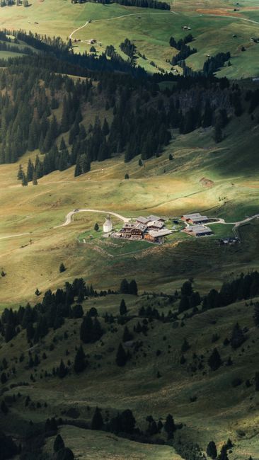 A picturesque aerial view of an alpine village surrounded by lush green mountains and rolling hills.