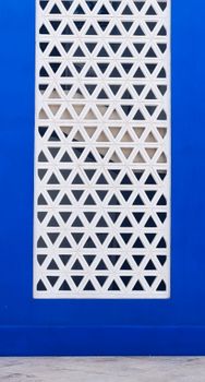 Abstract geometric window design on a bright blue wall, highlighting modern architectural style.