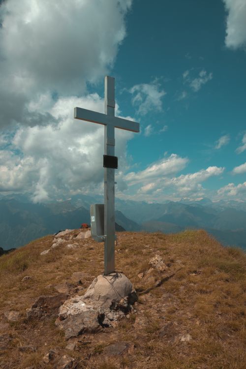 Free Tall summit cross on a mountain peak with a stunning backdrop of clouds and sky. Stock Photo