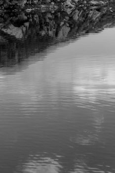 Serene lake with rippled surface and rocky reflection in black and white.