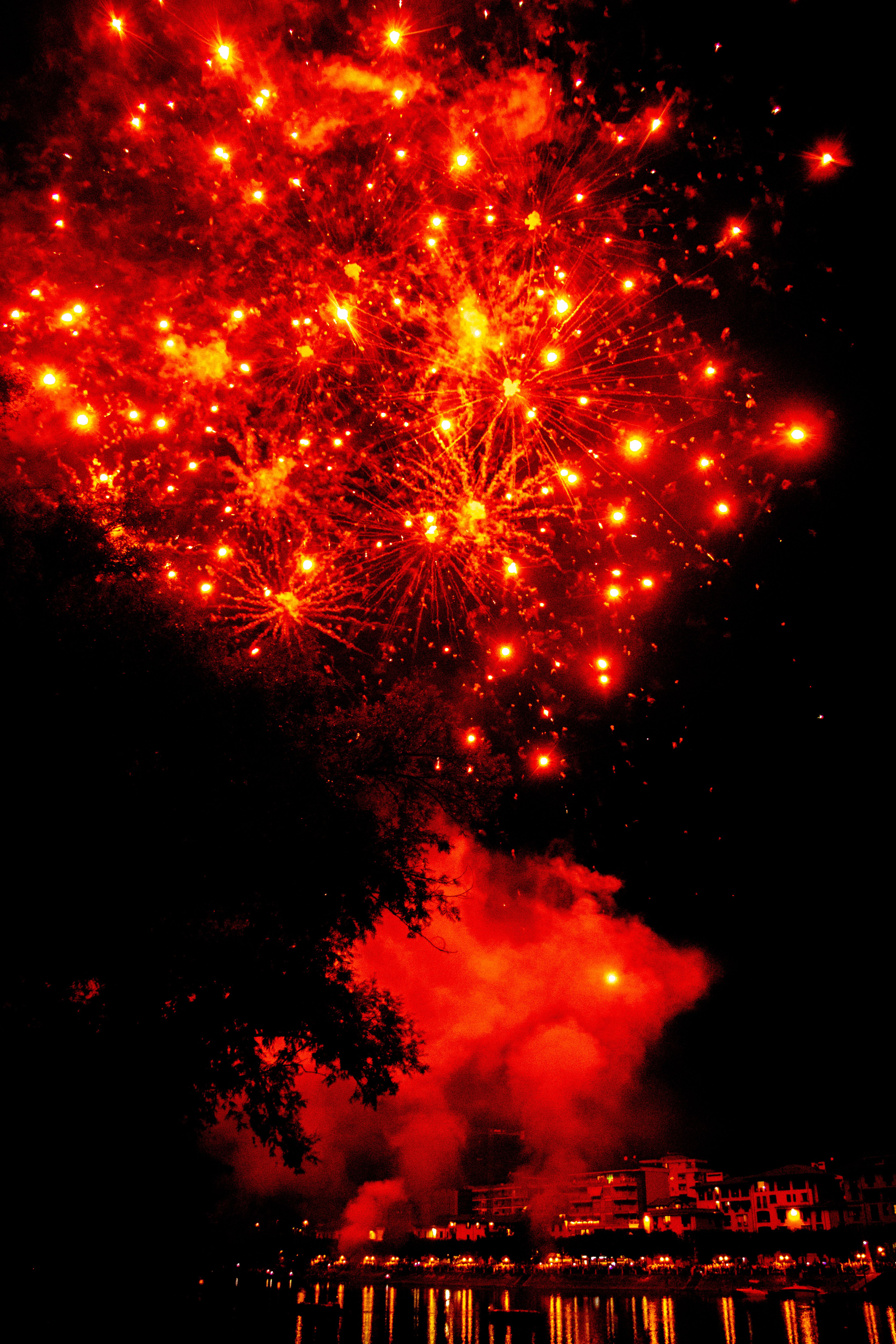 Fotomural Fuegos artificiales rojos vibrantes iluminan el cielo nocturno sobre un paisaje urbano.