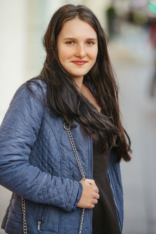 Free Stylish young woman wearing blue jacket, smiling outdoors on a bright day. Stock Photo