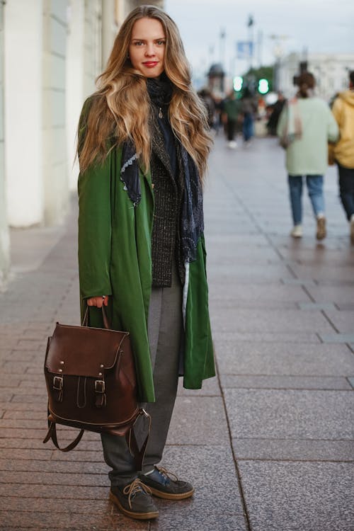 Blonde Woman in Green Coat Holding Leather Backpack Standing on Street