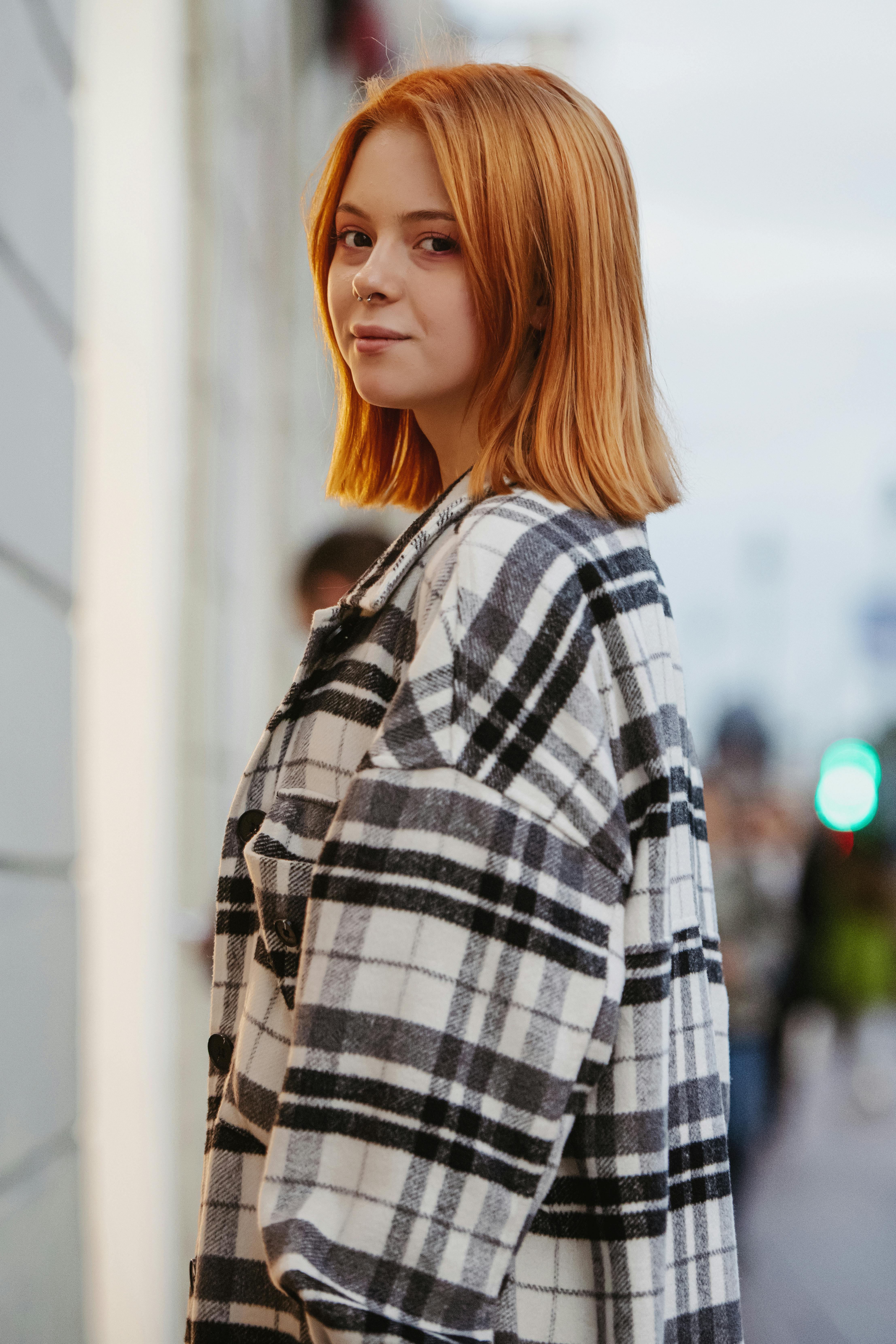 Portrait of a redhead woman in a checkered coat on an outdoor street setting.