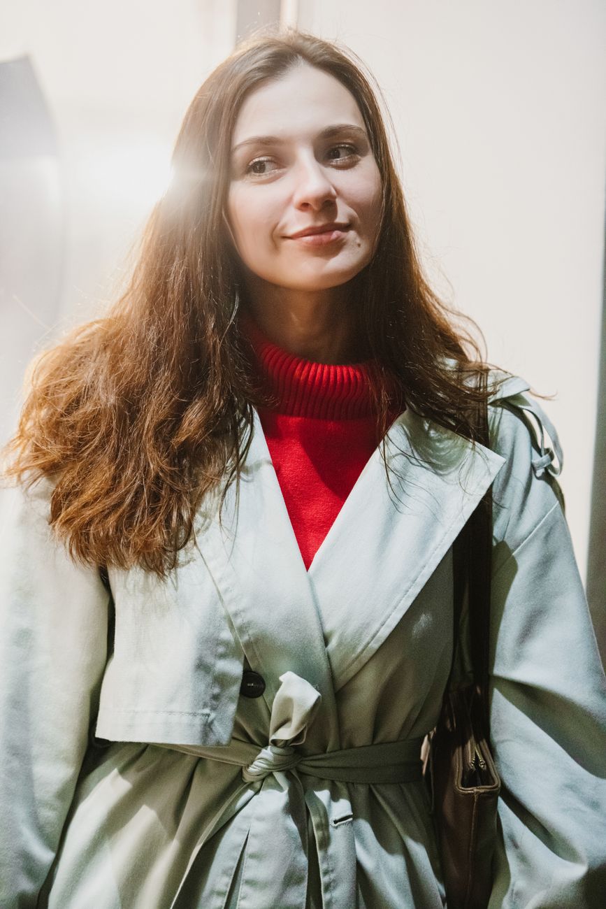 Young woman wearing a red turtleneck and coat, smiling under sunlight glow.