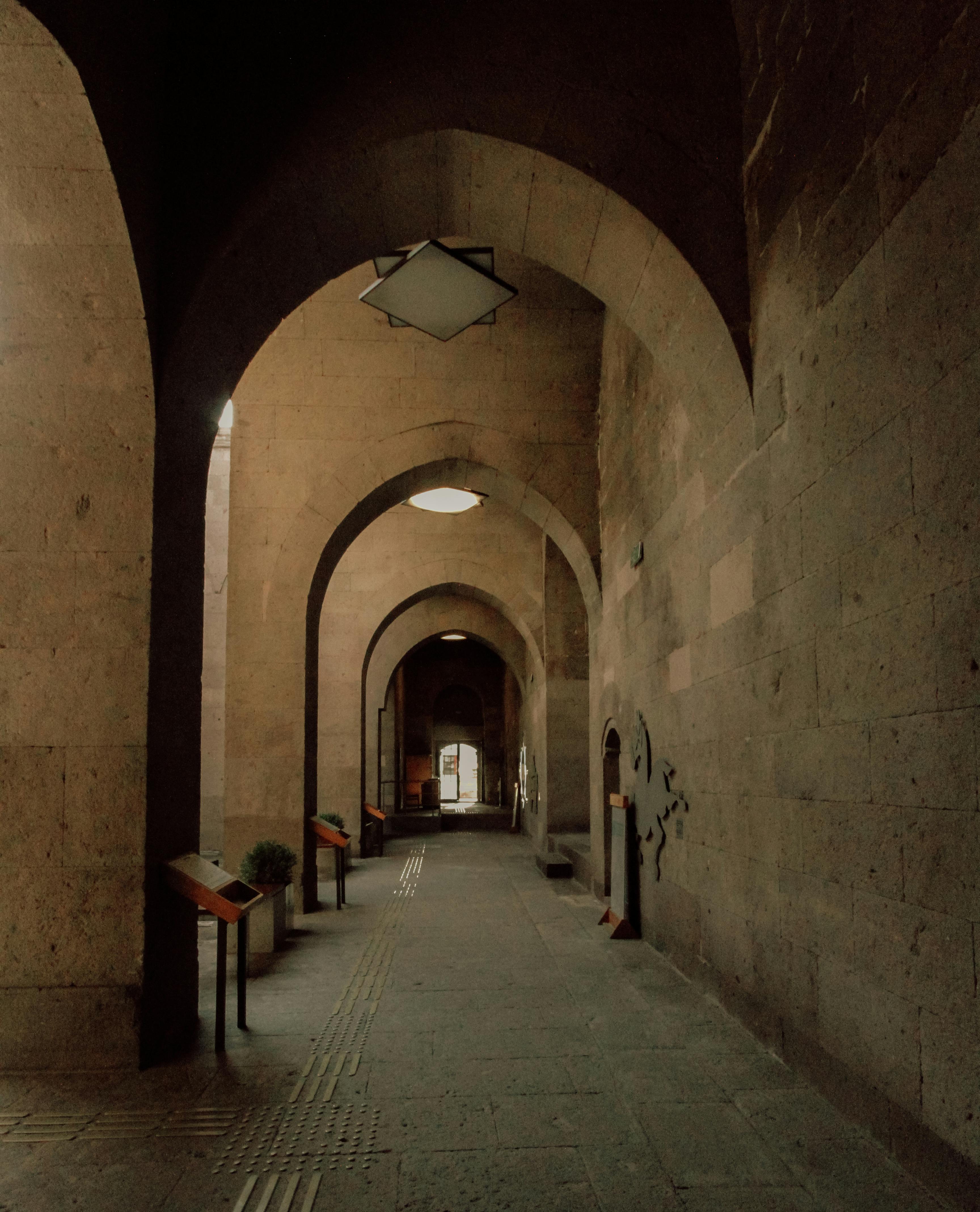 An atmospheric view of a stone passageway with arches and soft lighting, evoking historical architecture.