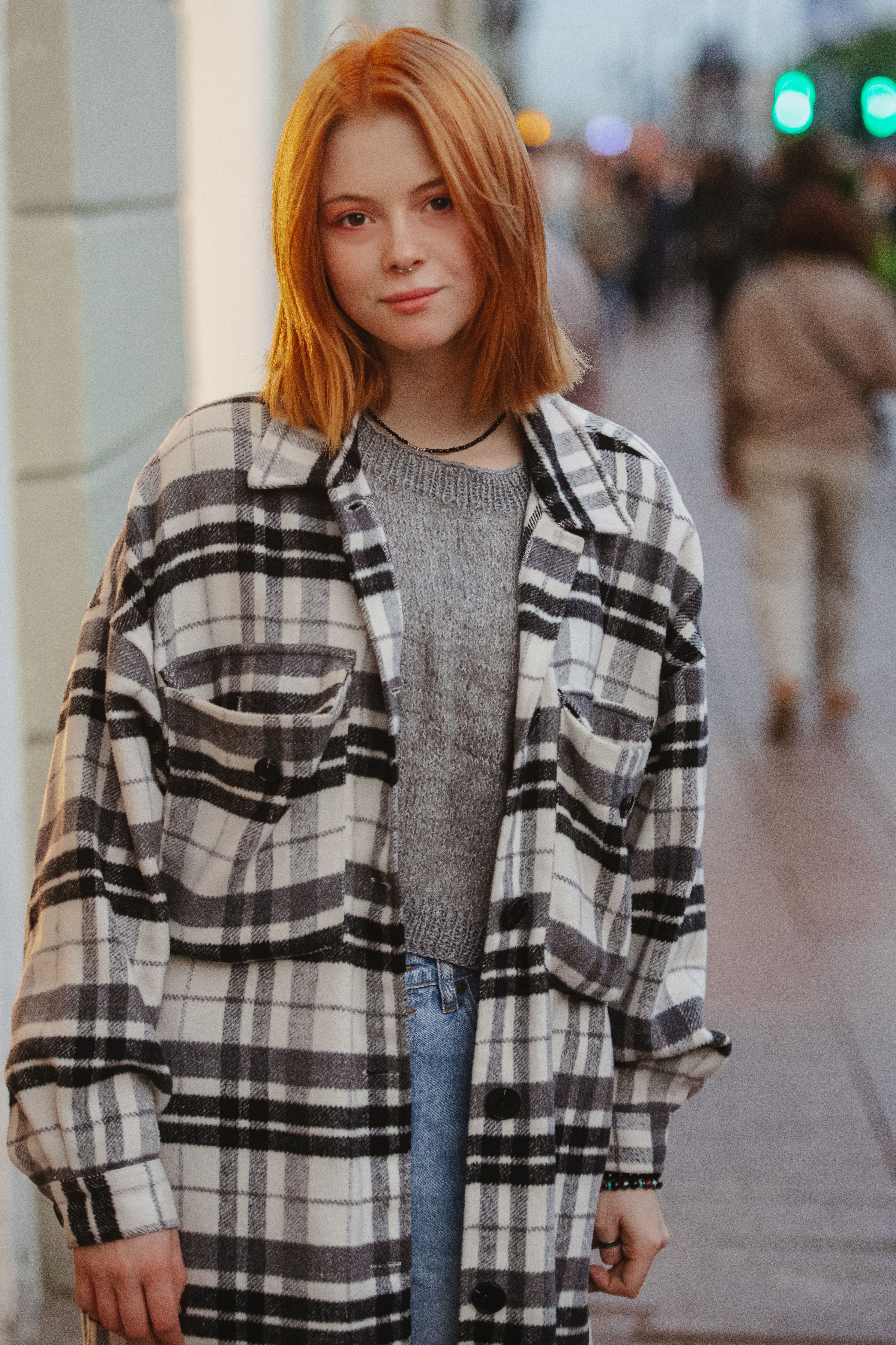 Fashionable redhead woman in a plaid coat posing confidently on a bustling city street.