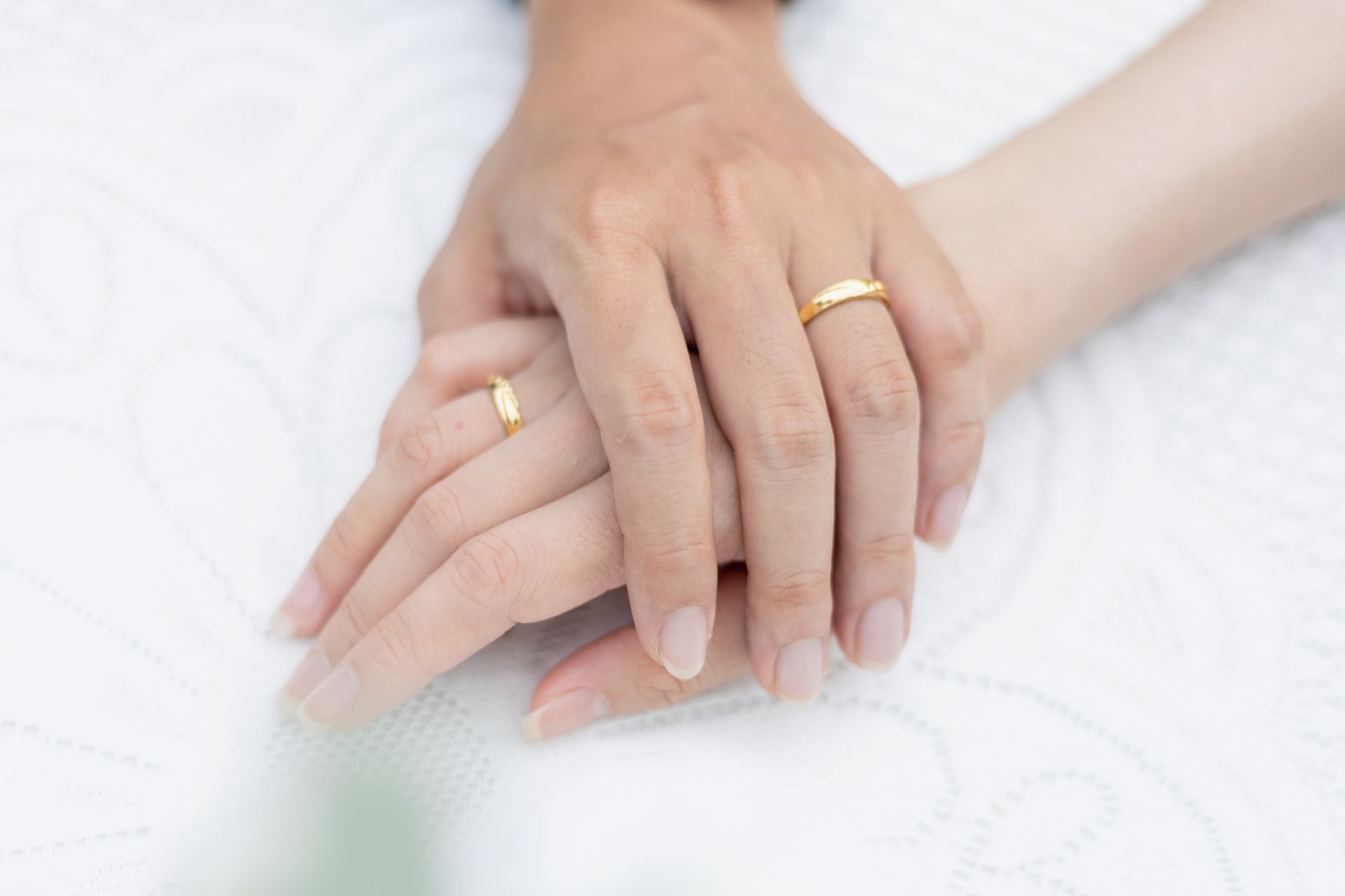 Close-up of two hands with gold rings on a white surface. Symbol of love and unity.
