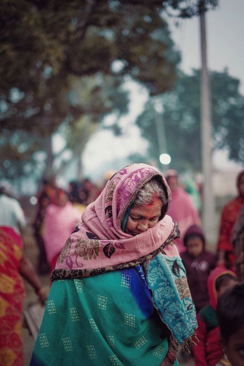 Free Portrait of an elderly woman in traditional clothing with a shawl, standing amidst a vibrant outdoor scene in Ghazipur, India. Stock Photo