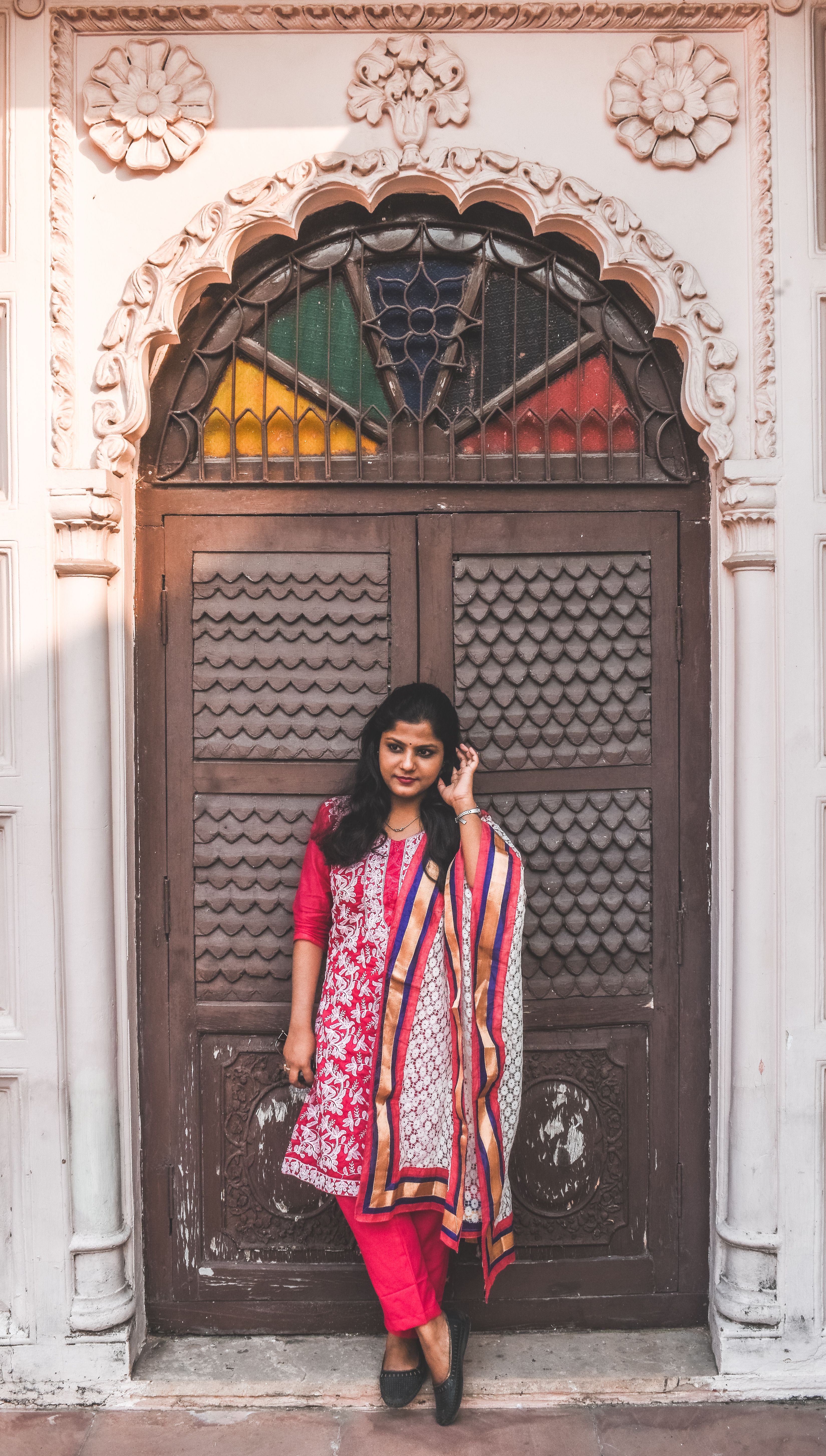 A woman in vibrant traditional Indian clothing stands elegantly by an ornate door in Varanasi, India.