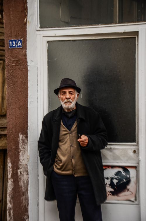 Free An elderly man with a gray beard and hat stands smoking by a doorway. Stock Photo