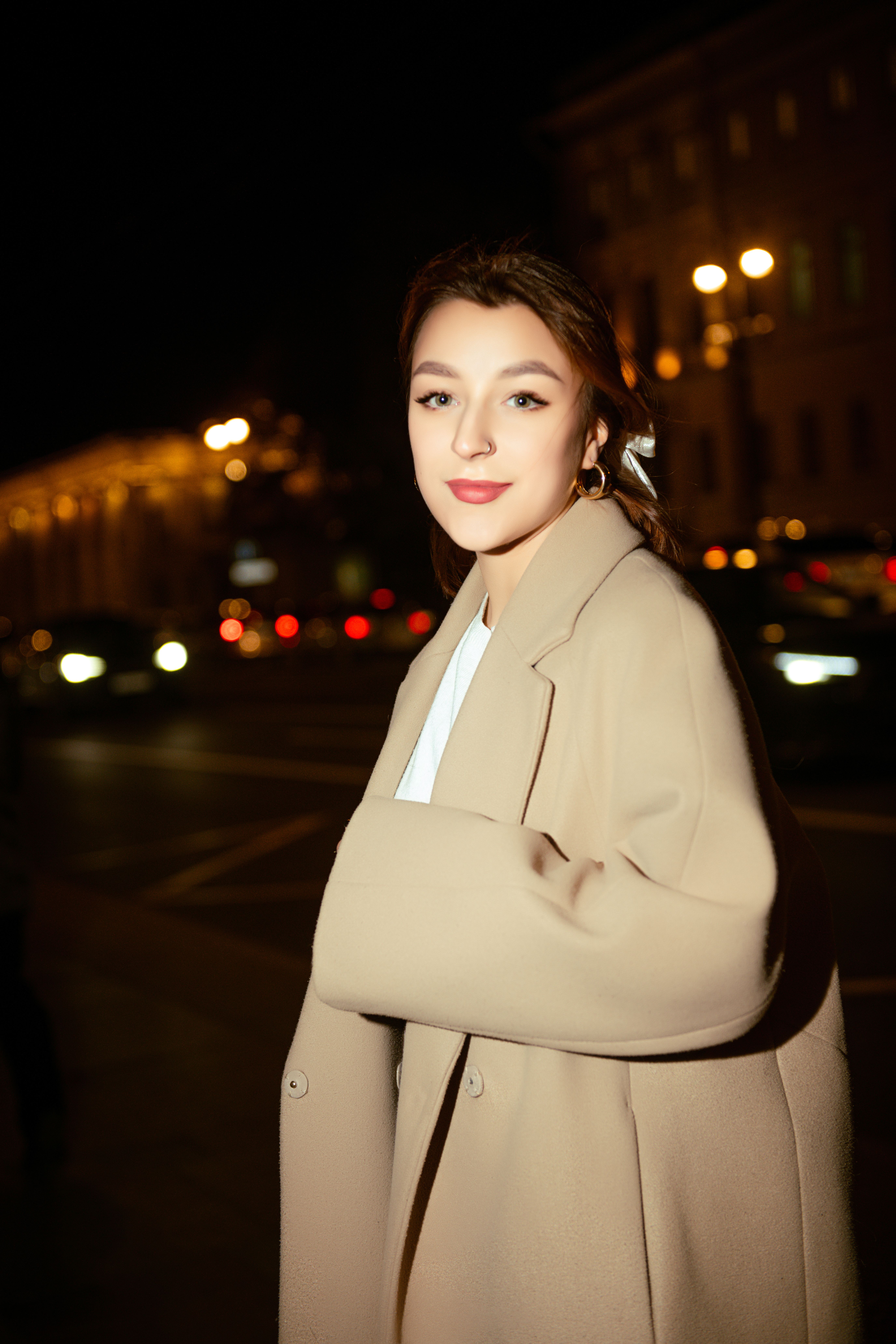 Portrait of a fashionable woman in a wool coat posing confidently at night in an urban environment.