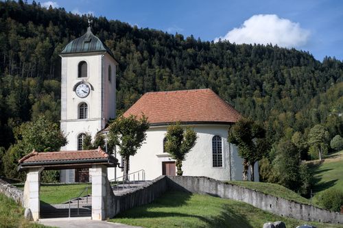 Free Beautiful church with clock tower in scenic Val-de-Travers, Switzerland, surrounded by lush hills. Stock Photo