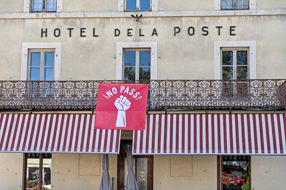Hotel De La Poste facade with striking protest banner reading 'No Pass' in Val-de-Travers, Switzerland.