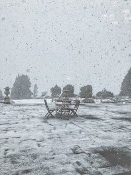 冬日庭院，积雪覆盖，桌椅静置，细雪纷飞