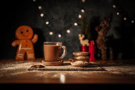 Warm hot chocolate with festive cookies and gingerbread man decor on a holiday table.