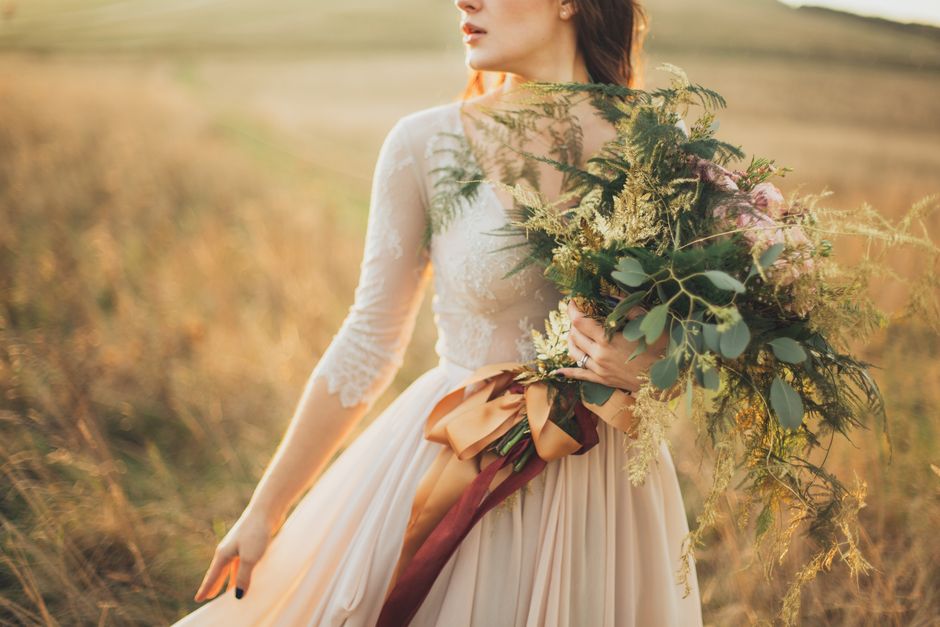 A romantic portrait of a bride holding a lush green bouquet in a peaceful golden field.