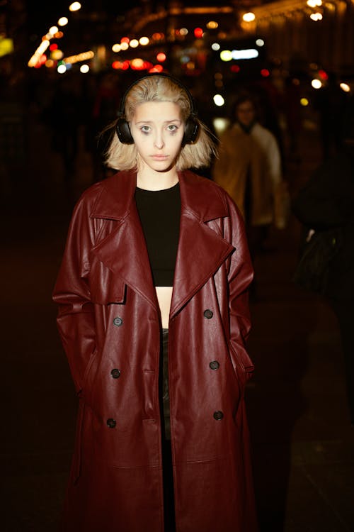 Young Woman in a Red Leather Coat Wearing Headphones and Standing Outside in the Dark 