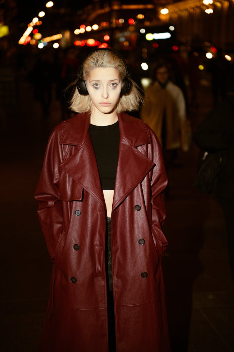 Young Woman In A Red Leather Coat Wearing Headphones And Standing Outside In The Dark 