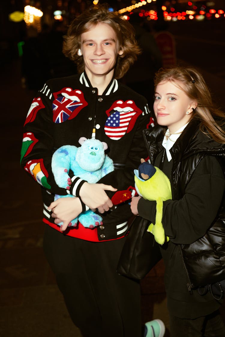 Young Man And Woman Standing Outside At Night And Holding Toys 