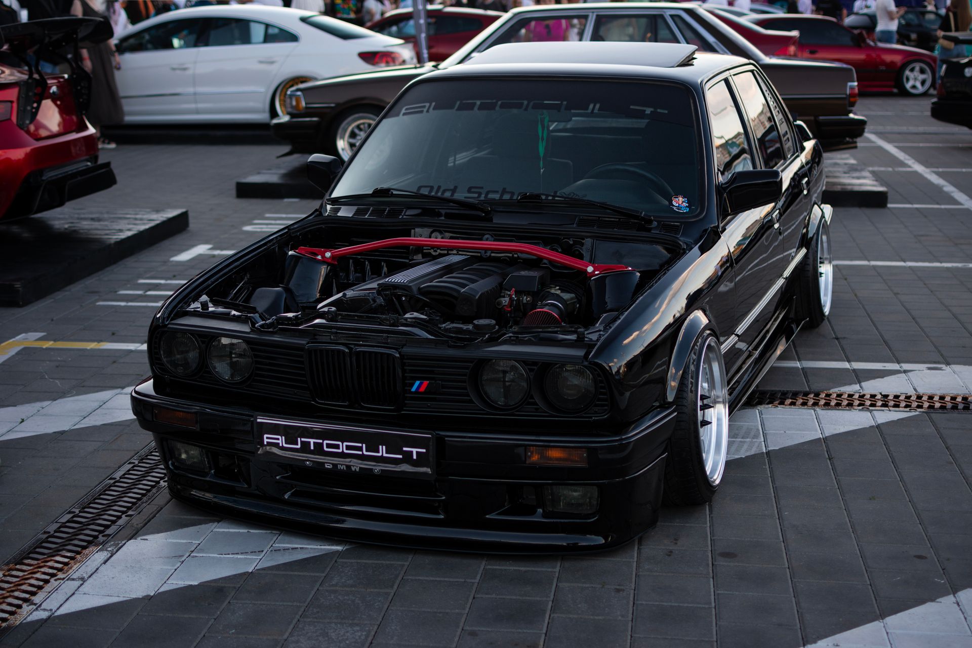 Sleek, customized black BMW E30 showcased at a bustling urban auto exhibition.