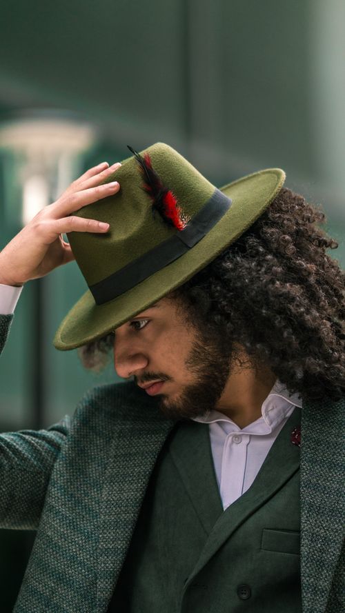 Free Portrait of a man with curly hair in green hat and suit, showcasing fashion elegance. Stock Photo