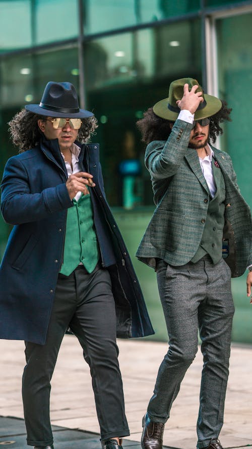 Elegant Men in Sunglasses and Hats Walking on a Sidewalk 